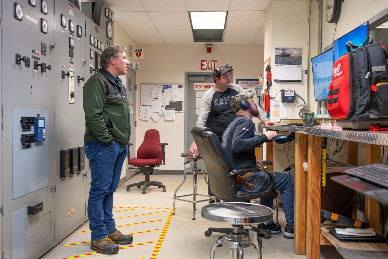 Three men looking at a screen in an electrical room.